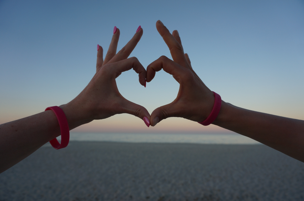 Hände von zwei LAUFMAMAs formen ein Herz am Strand